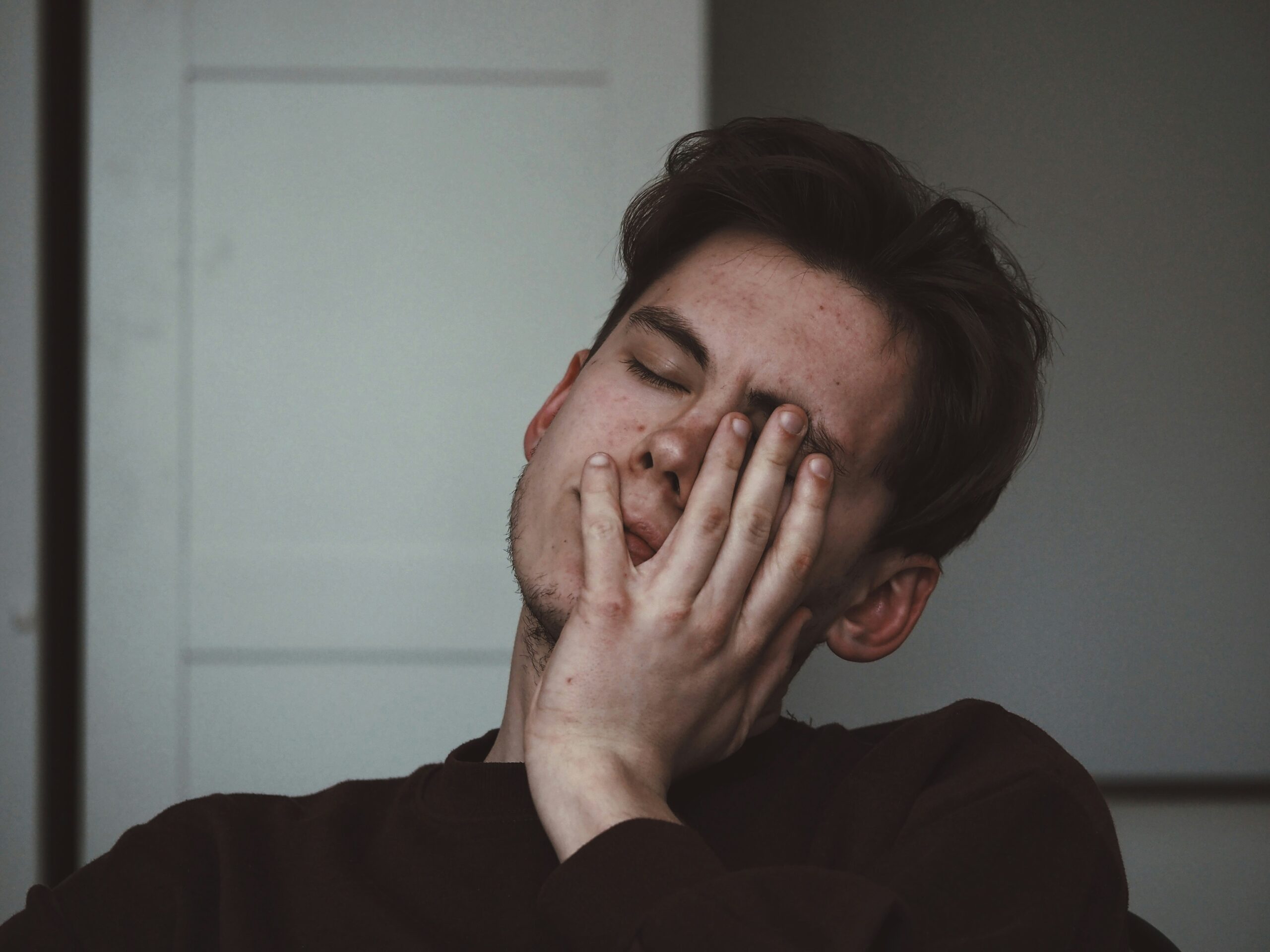 Exhausted man sitting on bed holding his head in the morning