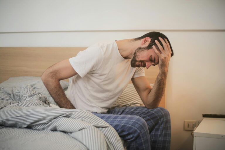 “Exhausted man sitting at his desk with his hand on his forehead, looking tired and stressed while working on his laptop